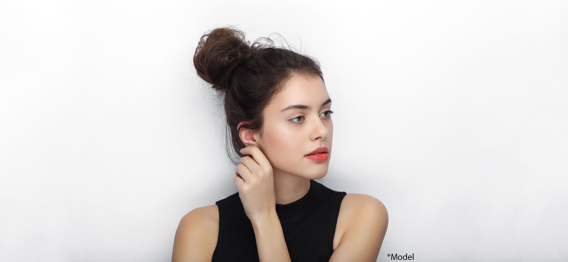 Beauty portrait of young adorable fresh looking brunette woman with high bun hairdo touching her ear